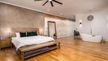 A modern bedroom with a large bed, a wooden bench, a bathtub, and a ceiling fan.