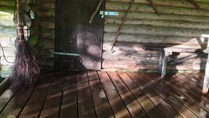 Una cabaña rústica de madera con una puerta de madera oscura, una escoba apoyada en la pared y un banco de madera.