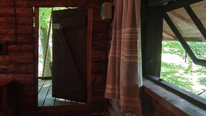 Una habitación de cabaña de madera con un ventanal grande, una puerta y una cama con una manta roja.