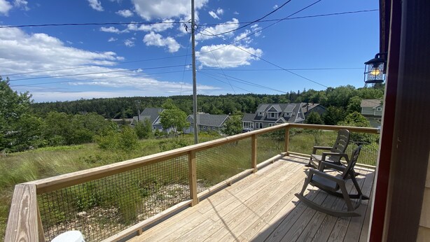 A wooden deck with a railing, a rocking chair, and a potted plant. - Acadia Birds Eye View Cottage (Southwest Harbor)