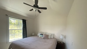 A bedroom with a bed, a ceiling fan, a window with curtains, and a nightstand with a lamp. - Acadia Birds Eye View Cottage (Southwest Harbor)