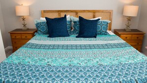Un lit recouvert d’une couvre-lit à motifs, deux oreillers foncés, une tête de lit en bois et deux tables de chevet ornées de lampes et de décorations en forme d’étoile.