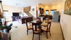 Un vaste espace de vie comprenant une table à manger, des chaises, un canapé, un téléviseur et un escalier menant à un autre niveau.