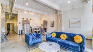 Ein geräumiger Wohnbereich mit einem blauen Sofa und Sesseln, einem Marmor-Couchtisch und einem Essbereich im Hintergrund.