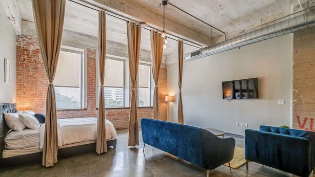 Ein modernes Hotelzimmer mit einem Bett, einer blauen Couch und einem großen Fenster mit Vorhängen.