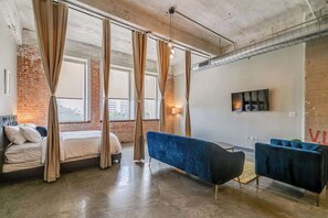 Ein modernes Hotelzimmer mit einem Bett, einer blauen Couch und einem großen Fenster mit Vorhängen.