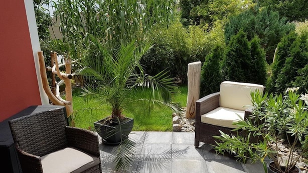 An outdoor patio with wicker furniture, potted plants, and a stone pathway.
