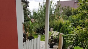 A garden pathway leading to a house with a white picket fence, surrounded by various plants and a stone pathway.