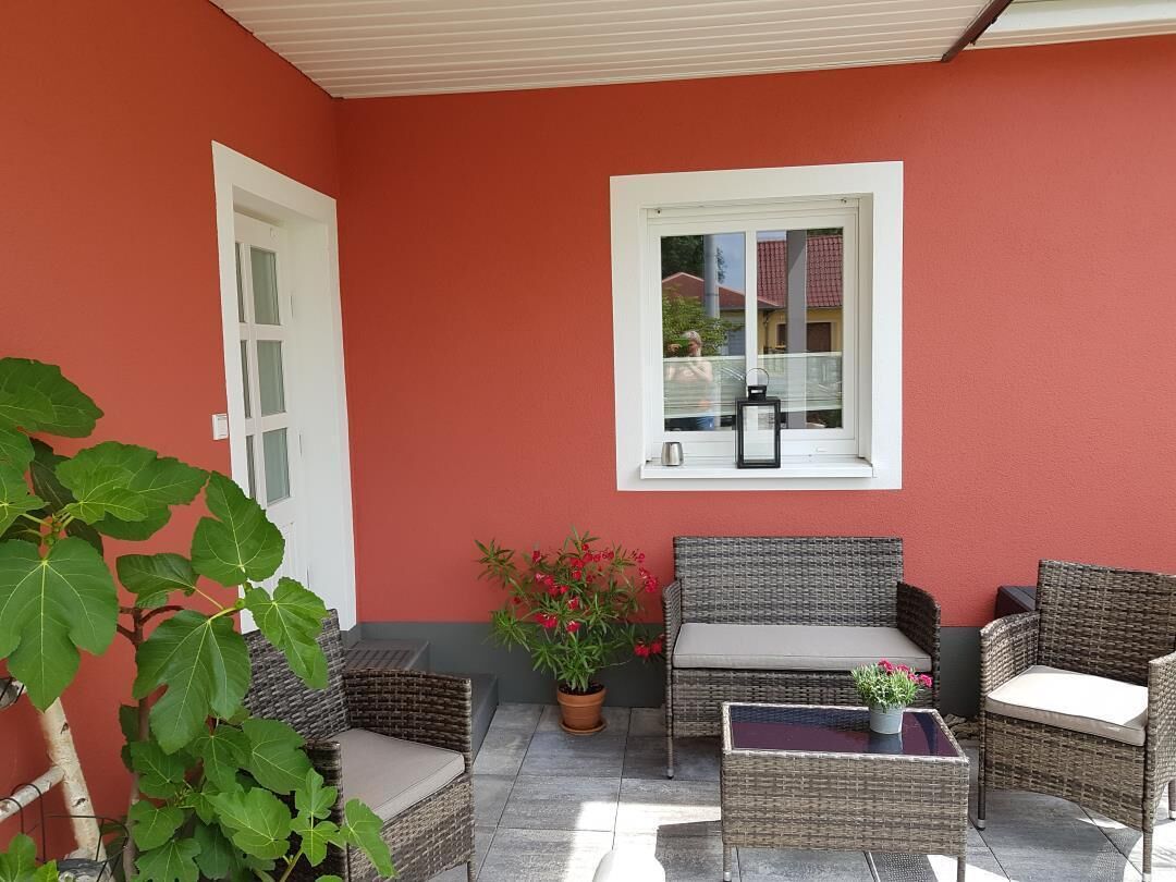 Un patio couvert aménagé avec des meubles en osier, une plante en pot et une fenêtre donnant sur un immeuble.
