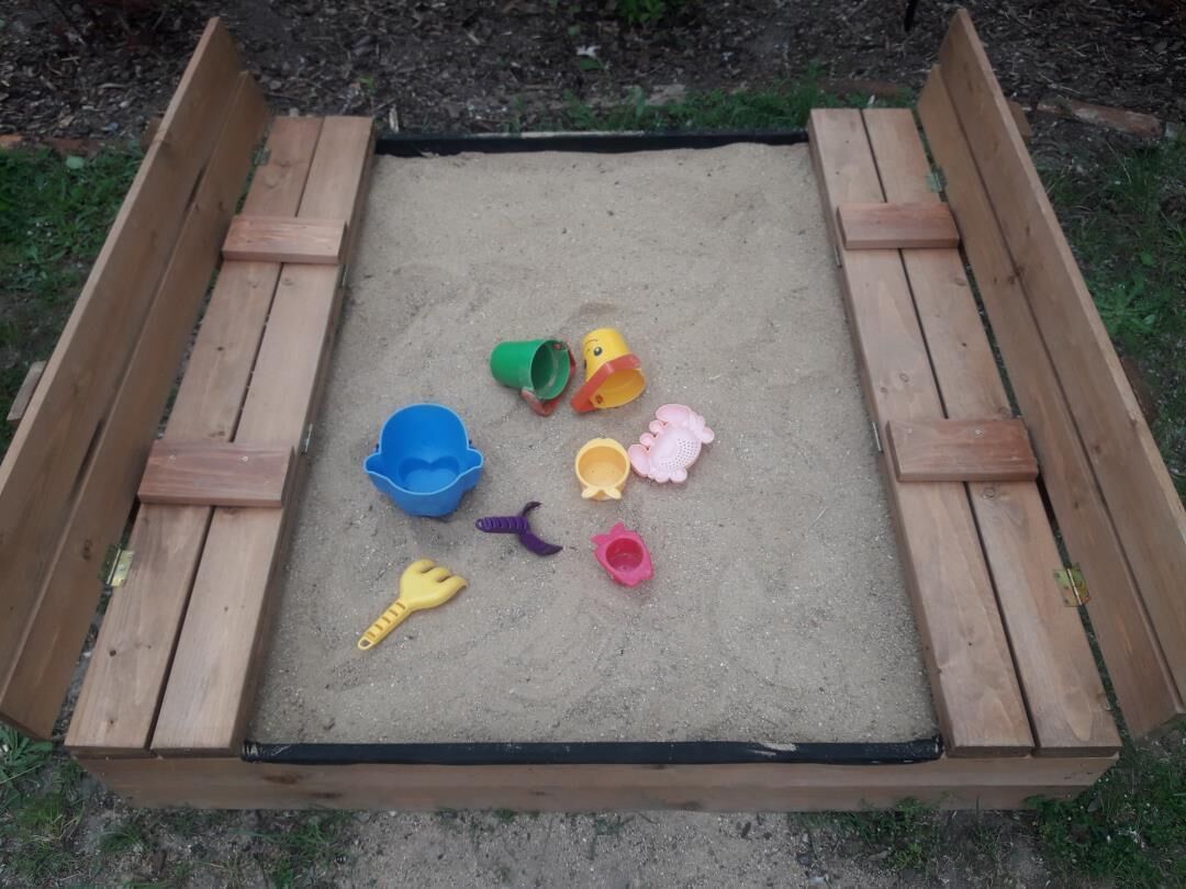 Un bac à sable avec des bordures en bois et divers jouets en plastique de couleurs vives.