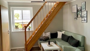 A living room with a wooden staircase, a green patterned sofa, a white coffee table, and framed pictures on the wall.