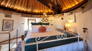 Een slaapkamer met een houten plafond, een bed met metalen frame, een nachtkastje en een lamp.
