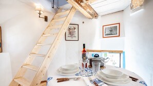 Een eetruimte met een houten ladder, witte muren, ingelijste foto's en een tafel gedekt met borden, glazen en bestek.