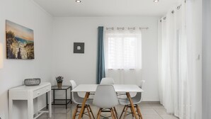Ein moderner Essbereich mit einem weißen Tisch und Stühlen, einem kleinen Beistelltisch mit Korb und Pflanze sowie einem Gemälde an der Wand.