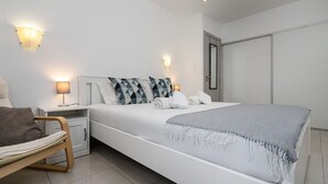Ein modernes Schlafzimmer mit einem großen Bett, Nachttischlampen, einem Sessel und einem Kleiderschrank.