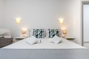 Quarto de hotel com uma cama grande, duas mesas de cabeceira, uma cadeira e duas luminárias fixadas na parede.