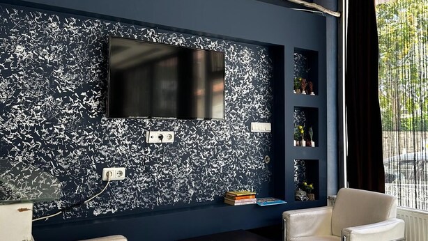 Una sala de estar moderna con una pared azul oscuro de acento, un televisor de pantalla plana, una mesa negra, dos sillones blancos y un ventilador de techo.
