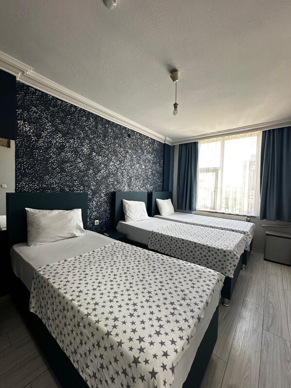 Habitación de hotel con tres camas, un muro oscuro con diseño y una ventana con cortinas.