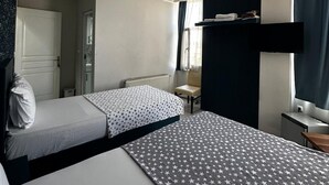 Habitación de hotel con dos camas, ventilador de techo, una mesita, una silla, ventana con cortinas y televisor instalado en la pared.