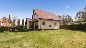 Une maison à deux étages, avec un toit recouvert de tuiles rouges, un petit porche et une pelouse bien entretenue.