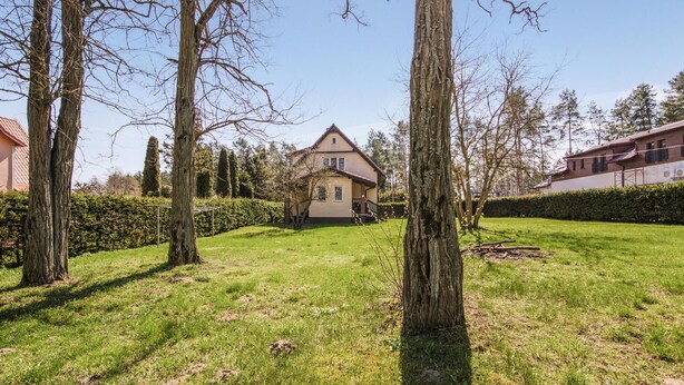Une maison avec un toit en pente, entourée d’une pelouse bien entretenue et de grands arbres.