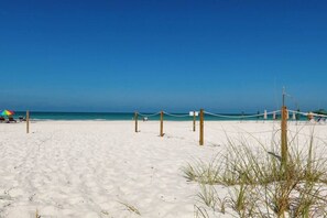 Ein Strand mit blauem Himmel, sandigem Ufer und einem Seilzaun.