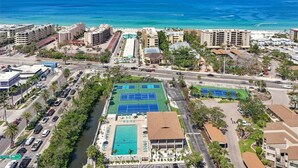 Vue aérienne d’un complexe hôtelier situé sur la côte, comprenant plusieurs bâtiments, une piscine, des courts de tennis et offrant une vue sur l’océan.