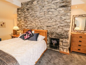 A bedroom with a stone wall, a bed with a white duvet, a wooden dresser, and a fireplace. - Hen Dy Craig Yr Ronwy (Bala)