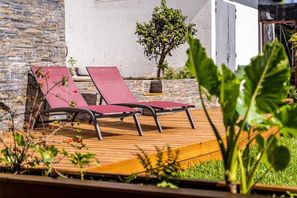 Dos sillones rojos en una terraza de madera con un muro de piedra y un árbol pequeño al fondo.