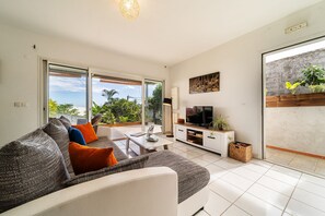 Una sala de estar moderna con sofá, televisor y balcón con plantas.