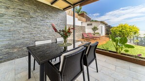 An outdoor patio with a stone wall, a table with chairs, and a view of a house and garden. - seasonal rental for 4 people max in large independent garden level (Saint Paul)