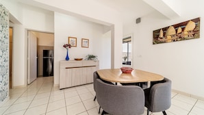 A modern kitchen with a dining area, featuring a wooden table and grey chairs, a vase with flowers, and framed pictures on the wall. - seasonal rental for 4 people max in large independent garden level (Saint Paul)