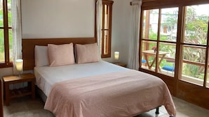 A bedroom with a bed, two bedside tables, a nightstand, a window with curtains, and an air conditioning unit. - GALAPAGOS SUITE VELERO (Puerto Ayora)