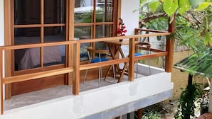 A wooden balcony with a small table and chairs, a railing, and a view of greenery. - GALAPAGOS SUITE VELERO (Puerto Ayora)