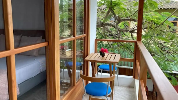 A balcony with a wooden table and chairs, a small potted plant, and a view of lush greenery. - GALAPAGOS SUITE VELERO (Puerto Ayora)
