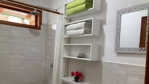 A bathroom with a shower, a sink, and a mirror. There are shelves with towels and a vase with flowers. - GALAPAGOS SUITE VELERO (Puerto Ayora)