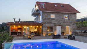 Una casa de piedra con piscina, mobiliario exterior y zona de barbacoa.