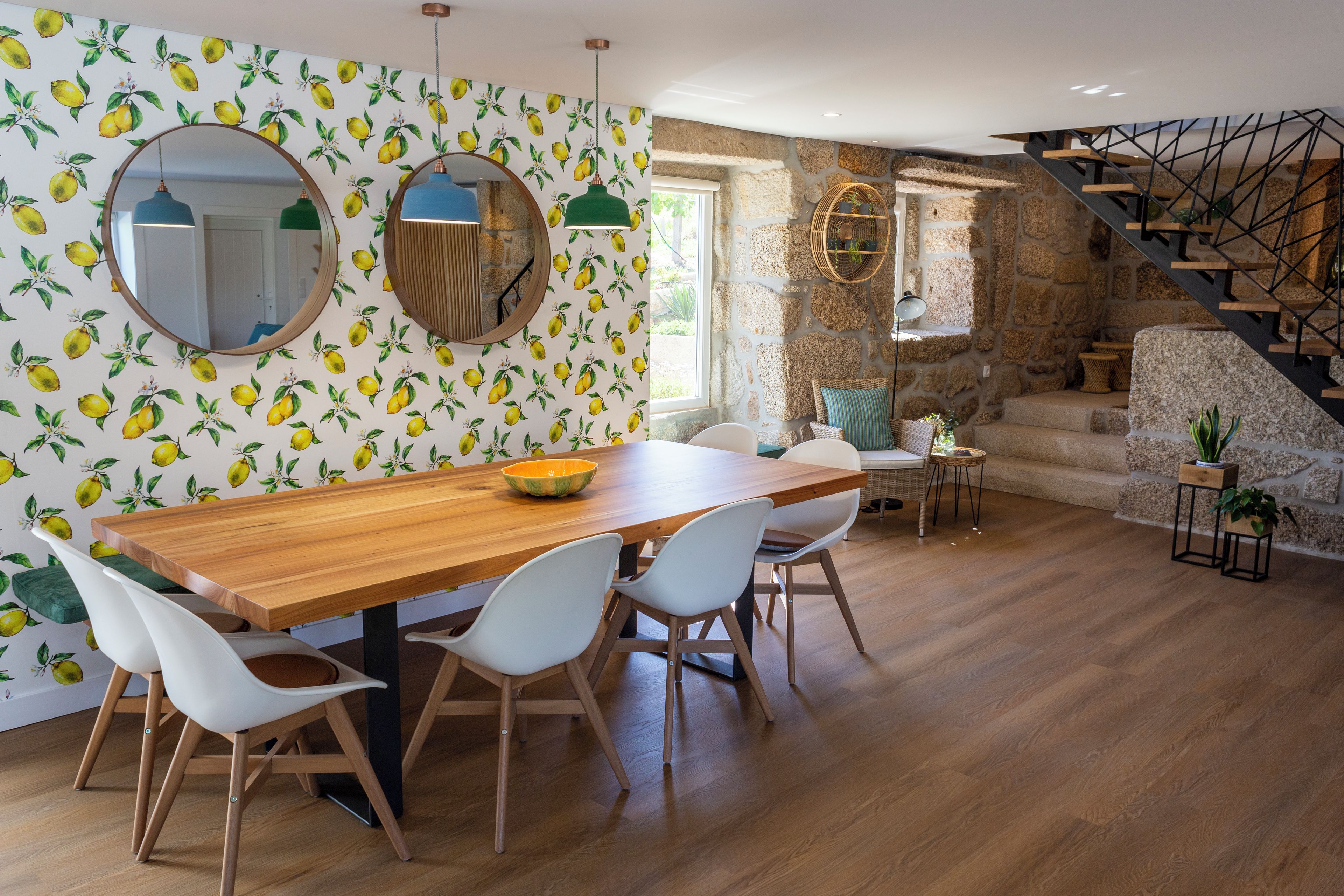 Un comedor con una mesa de madera y sillas blancas, una pared de piedra y una escalera.