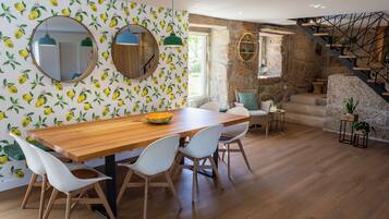 Un comedor con una mesa de madera y sillas blancas, una pared de piedra y una escalera.
