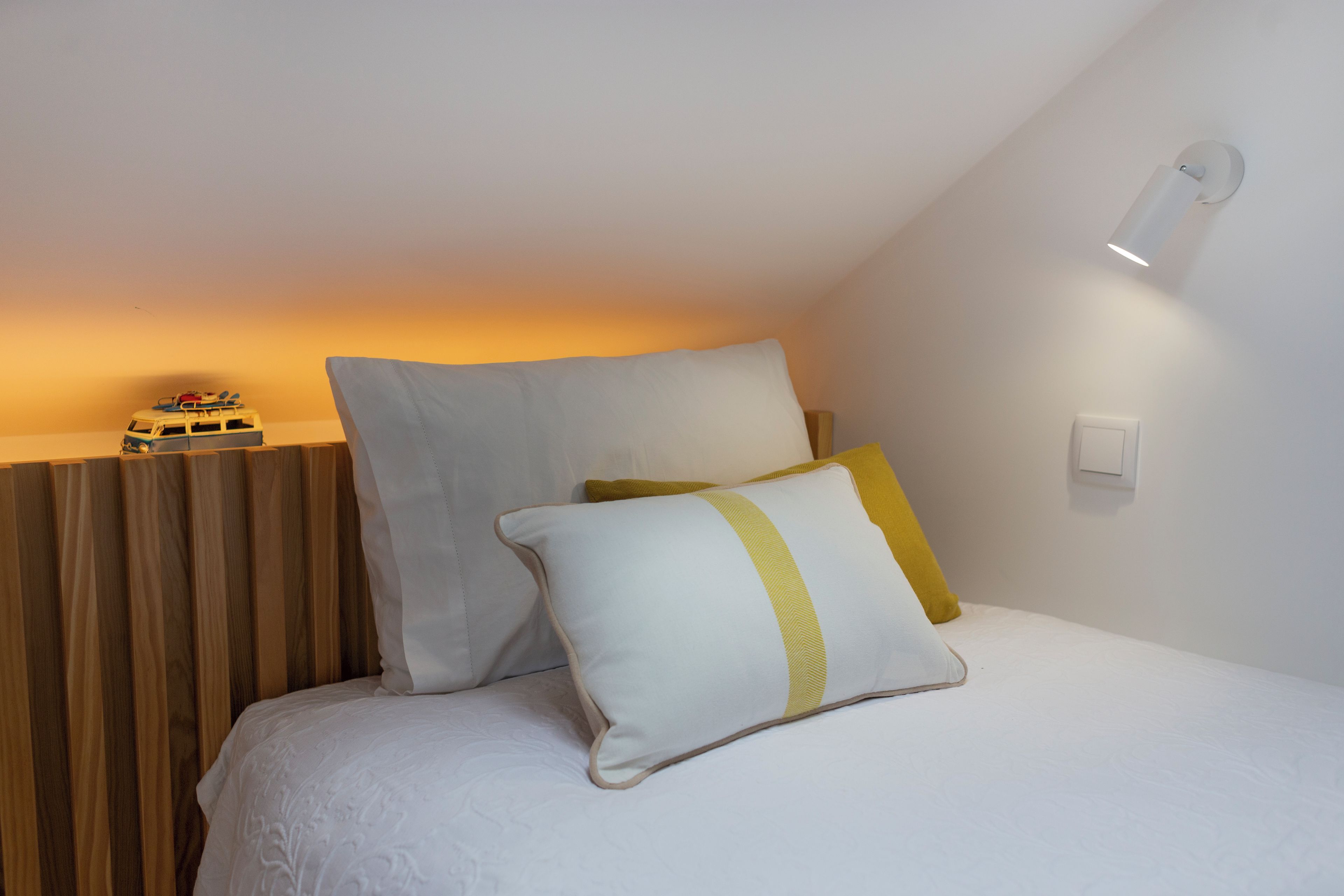 Un dormitorio con cama, almohadas, una mesita de noche y una lámpara de pared.
