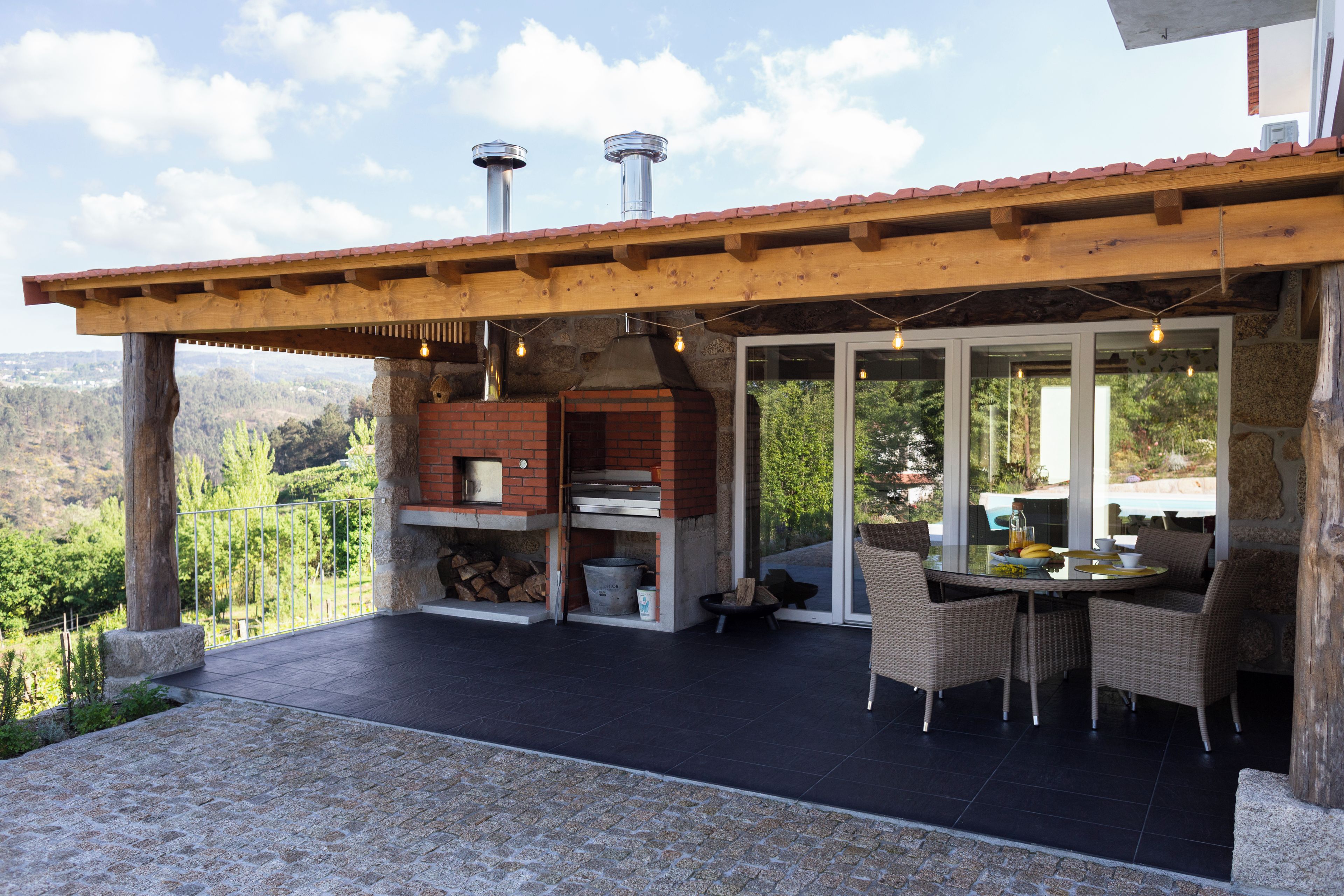 Un patio con horno de ladrillo, mobiliario de mimbre y vista al paisaje.