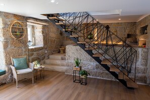A modern interior with a stone wall, a wooden staircase, a wicker chair, and a small table with a plant.