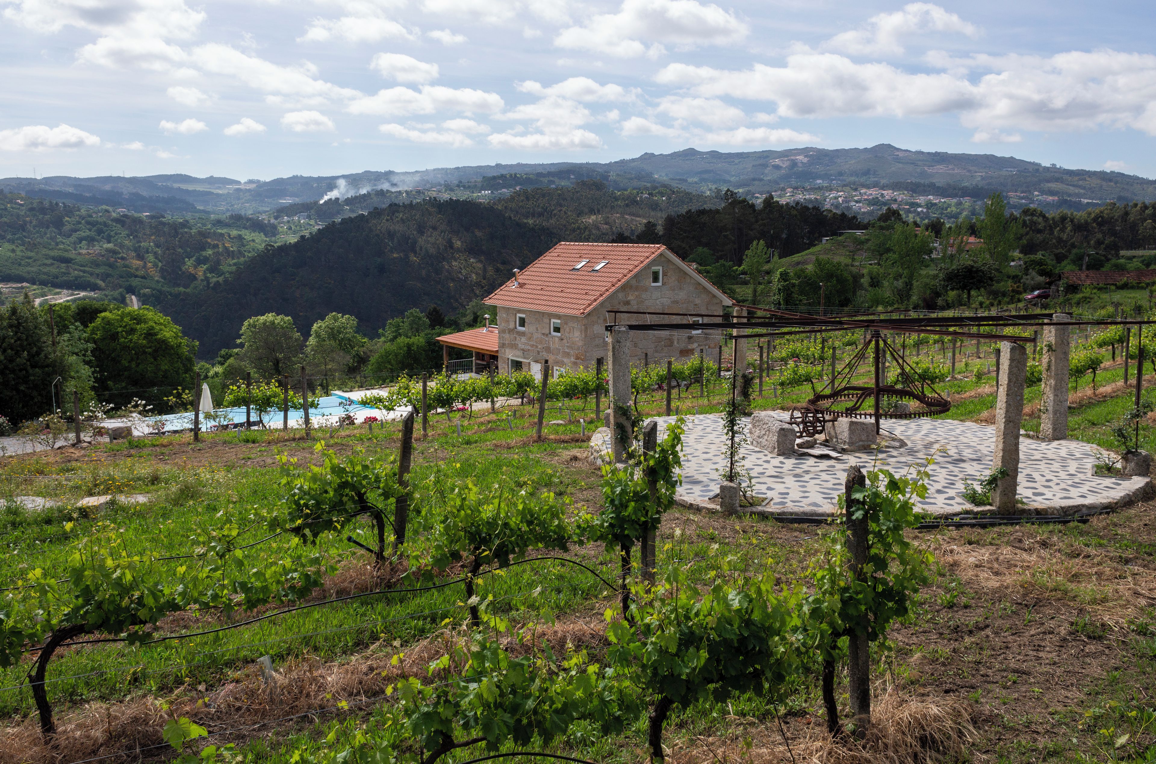 Viñedo con un edificio de piedra, un patio circular de piedra y montañas al fondo.