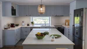 Una cocina moderna con armarios grises, una isla central con un frutero, un refrigerador de acero inoxidable y una ventana con vistas al exterior.