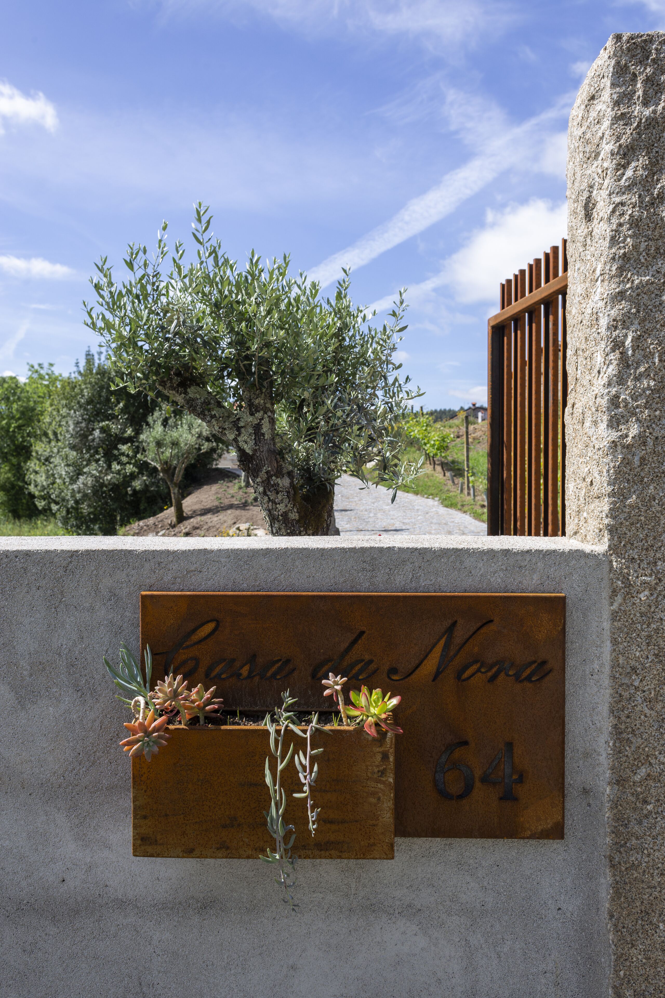 Una señal con el texto 'Casa da Nona 64' colocada en una pared, con una jardinera pequeña que contiene suculentas.
