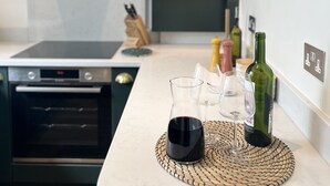 Ett modernt kök med en inbyggd ugn, en köksfläkt i rostfritt stål och en bänkskiva med en vävd bordstablett som håller vinglas och en vinflaska.