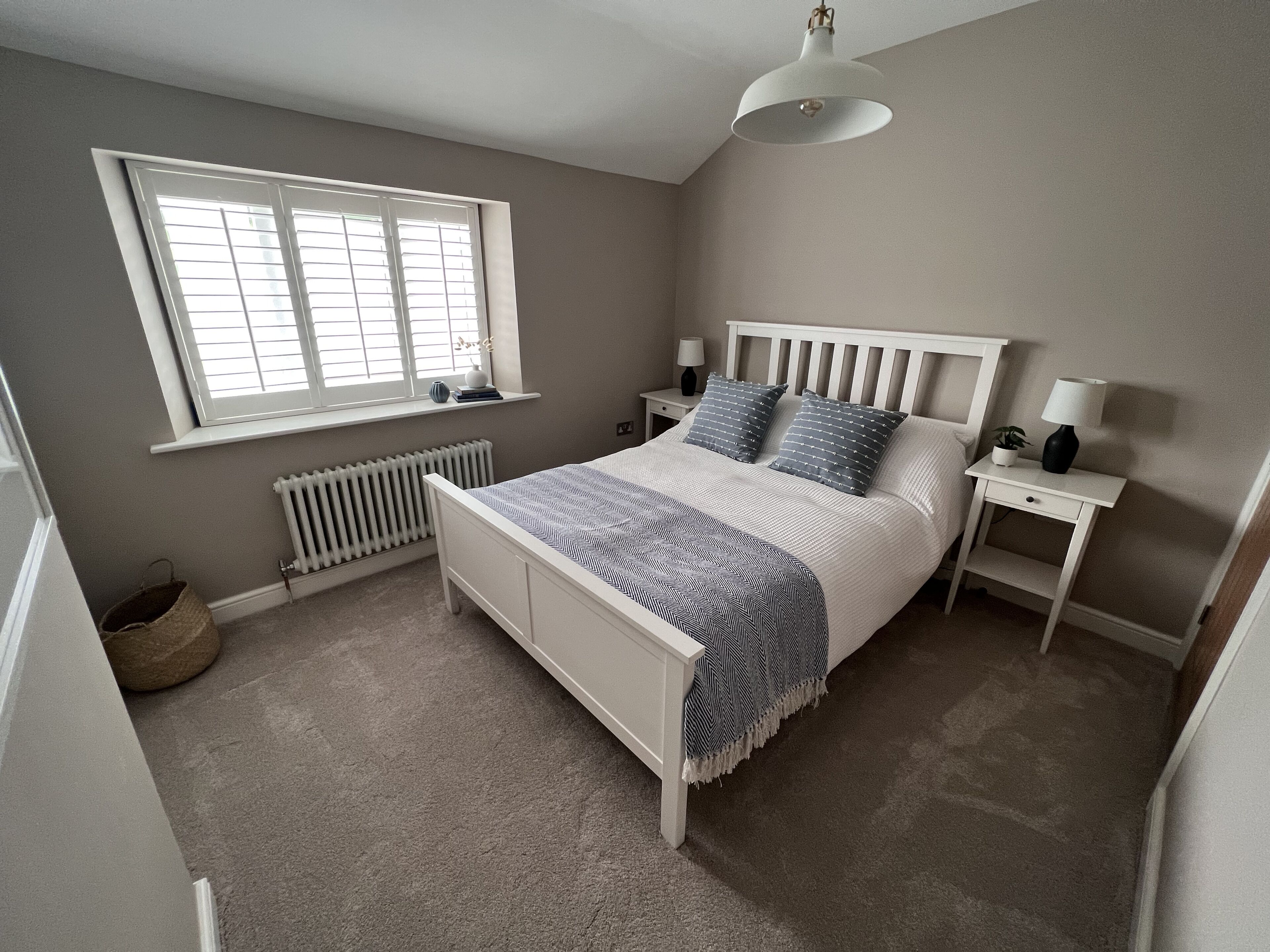 Quarto com cama, mesas de cabeceira, janela e radiador.
