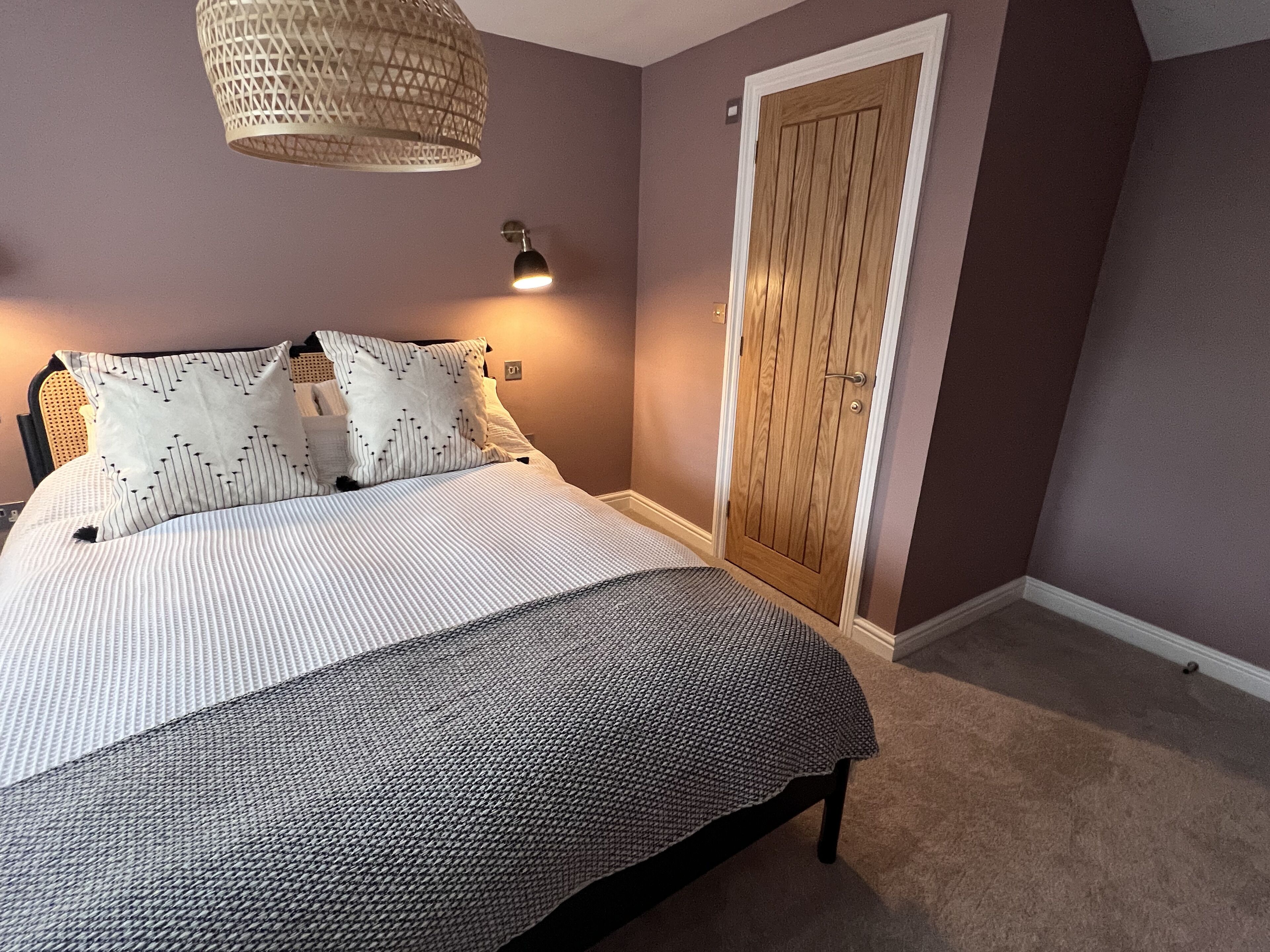 A bedroom with a bed, a hanging light fixture, a door, and a carpeted floor.