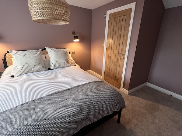 A bedroom with a bed, a hanging light fixture, a door, and a carpeted floor. - Cosy Lake District Cottage (Staveley)