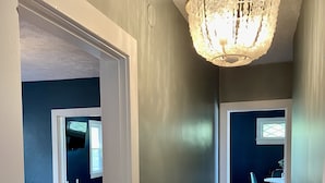 Un couloir doté d’un plancher en bois, d’un lustre et d’un coin repas avec des chaises et une table.